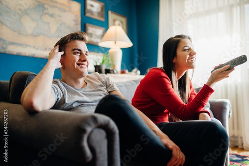 Couple at home watching TV.Remote control fight won by girlfriend.Boyfriend bored by TV program.Watching her favorite show/film.Chick flick movie.Binge watching television.Relationship home problems.