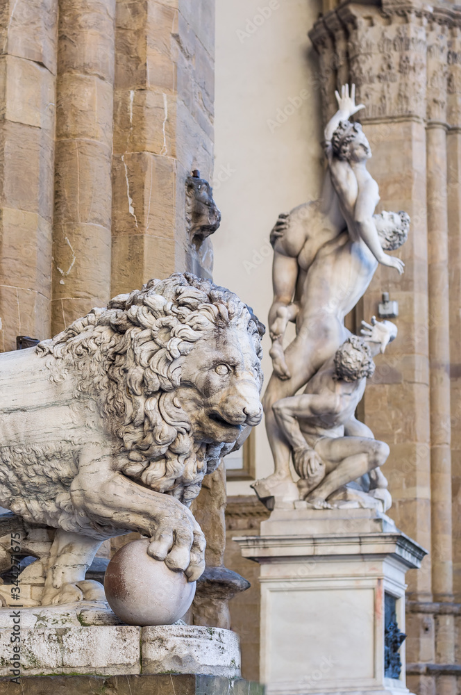 Fancelli's ancient lion - Medici lion. Marble sculpture displayed at the Loggia dei Lanzi. The Rape of the Sabine Women on background. Piazza della Signoria, Florence, Italy. Focus on foreground.