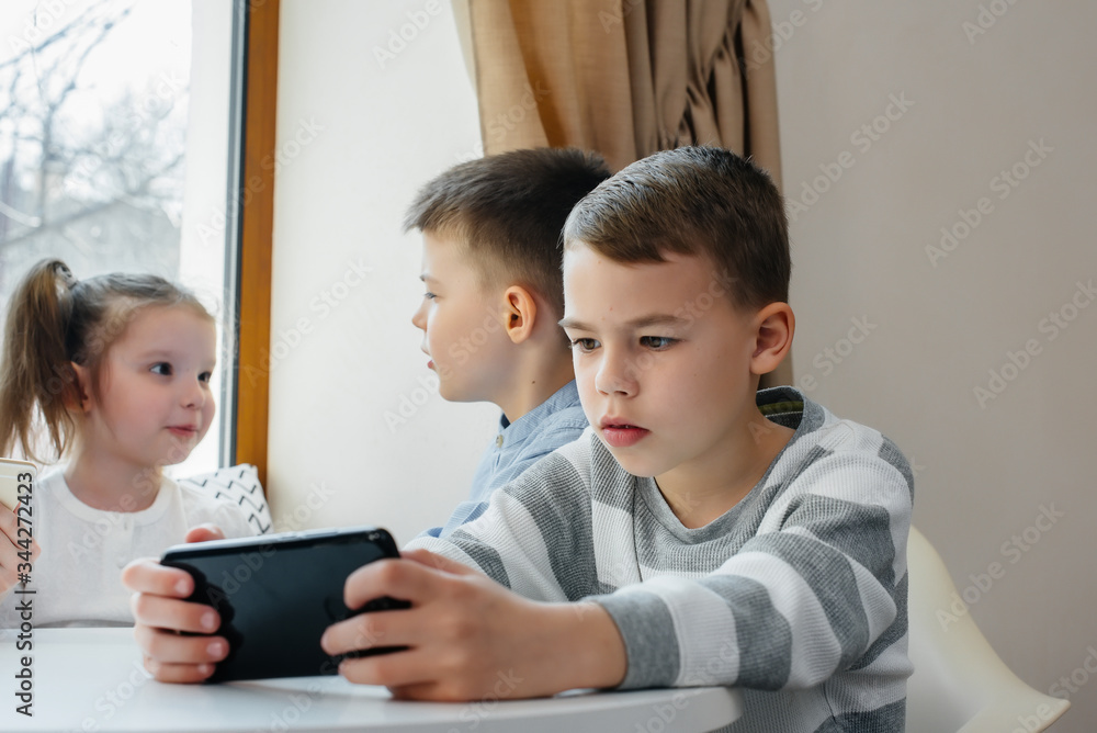 Children sit at a table in a cafe and play mobile phones together. Modern entertainment Children sit at a table in a cafe and play mobile phones together. Modern entertainment