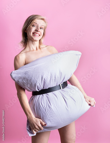 young beautiful woman dressed in pillow smiling isolated on pink background photo