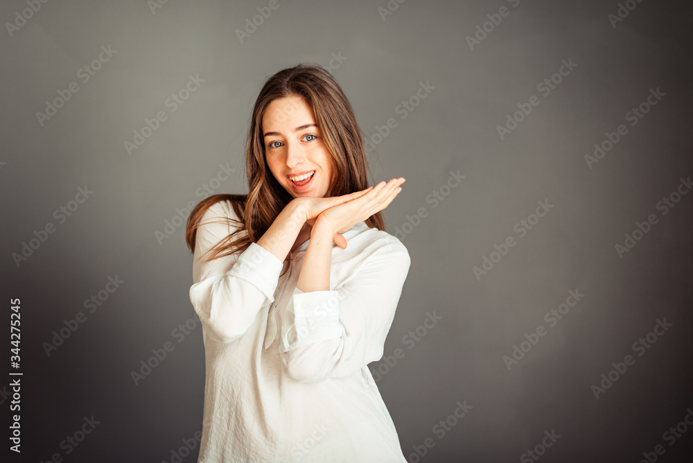 Young girl in a white shirt, hands up, on a gray background. Honest and emotional on the banner, billboard, billboard. No retouch. Without make-up. Young girl in a white shirt, hands up, on a gray background. Honest and emotional on the banner, billboard, billboard. No retouch. Without make-up.