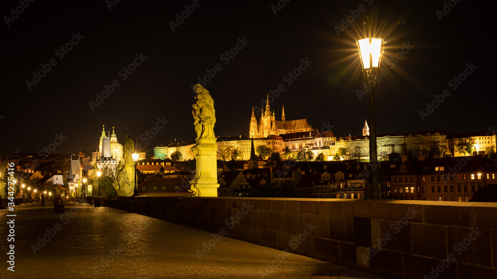 Panoramic view of Prague skyline at night. Statues and gas lamps on the Charles bridge and Prague Castle with spires of St. Vitus cathedral in background