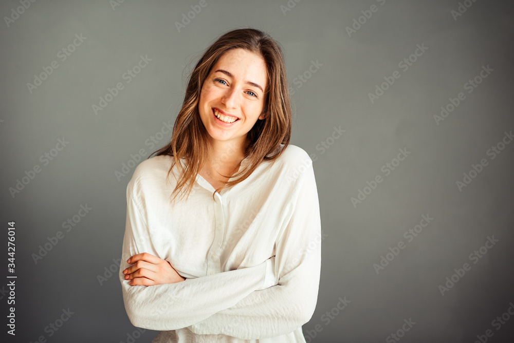 Obraz premium Young girl in a white shirt, hands up, on a gray background. Honest and emotional on the banner, billboard, billboard. No retouch. Without make-up.