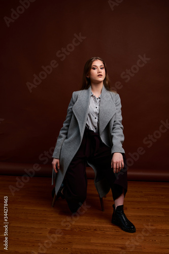 Independent young woman posing in the photostudio. Gorgeous young female in classic suit and grey coat.