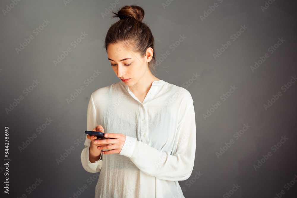 Serious girl with blindfolded hair on her head. With a phone in his hands. Portrait. On a gray background. Without makeup, without retouching. Serious girl with blindfolded hair on her head. With a phone in his hands. Portrait. On a gray background. Without makeup, without retouching.