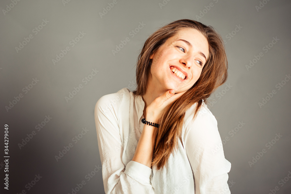 Smiling girl with a satisfied face hands near the face on a gray background, close-up. Nude makeup, without retouching. Smiling girl with a satisfied face hands near the face on a gray background, close-up. Nude makeup, without retouching.