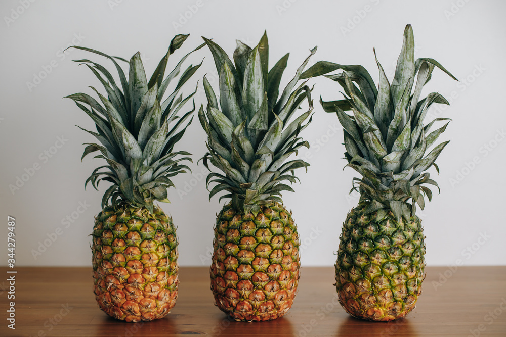 Three pineapples stand on a wooden table. Pineapples and cactus fruits are on the table. Exotic fruits.
