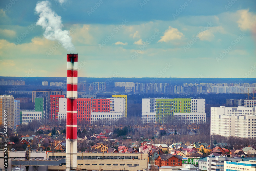 Single-storey houses surrounded by high-rise buildings. Factory chimney on the background of the city from which smoke is coming