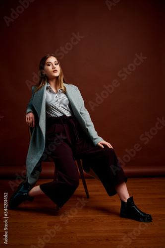 Independent young woman posing in the photostudio. Gorgeous young female in classic suit and grey coat.