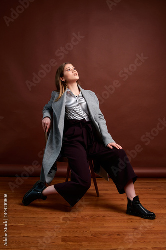 Independent young woman posing in the photostudio. Gorgeous young female in classic suit and grey coat.