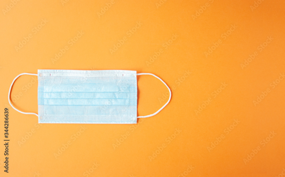 Disposable medical mask on orange backggroun against bacteria and viruses. Stop the spread of coronavirus, self-defense. Copy space Disposable medical mask on orange backggroun against bacteria and viruses. Stop the spread of coronavirus, self-defense. Copy space