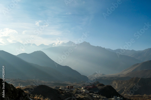 Himalayan chains shrouded in fog  seen from Muktinath  Annapurna Circuit Trek  Nepal. There are multiple mountain chains. Sunbeams breaching through the peaks. Golden hour. Meditation and serenity.
