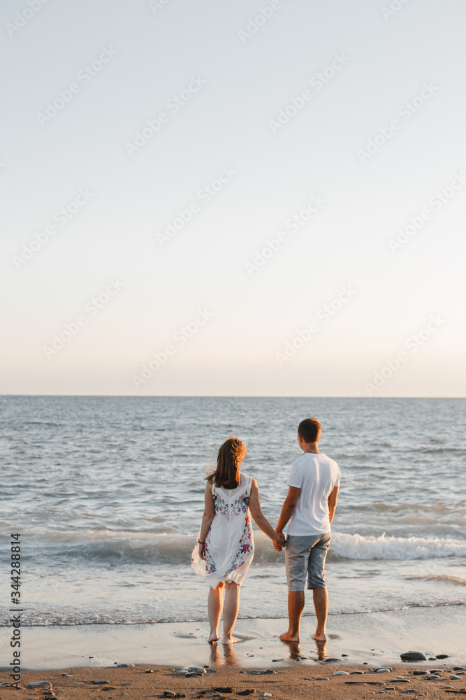 Young couple in love stand on the shore of the Black Sea on the wet sand and look into the distance at the horizon. Young couple in love stand on the shore of the Black Sea on the wet sand and look into the distance at the horizon.