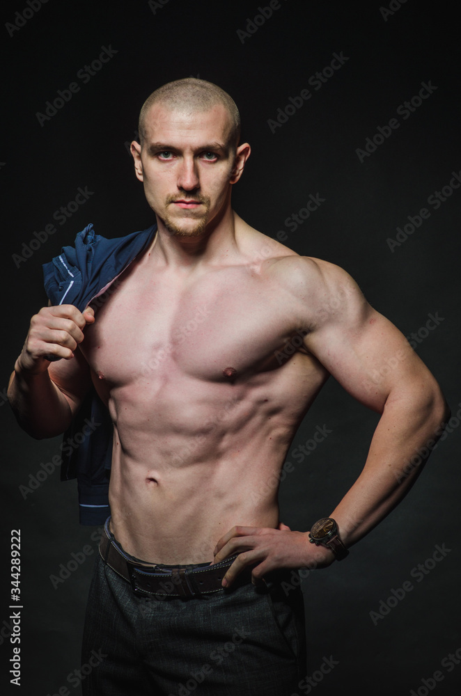 Fototapeta premium A stylish, bald young man stands with a naked torso on a dark background in the category