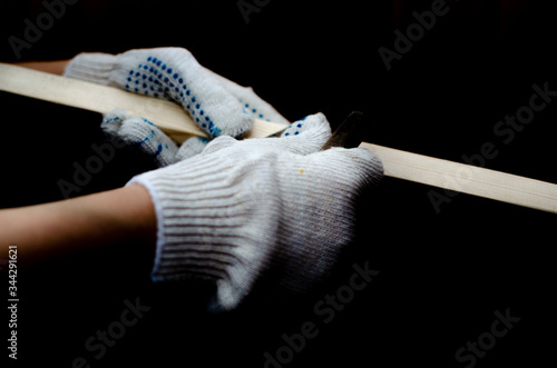 hands in construction gloves sanding wooden beam on black background