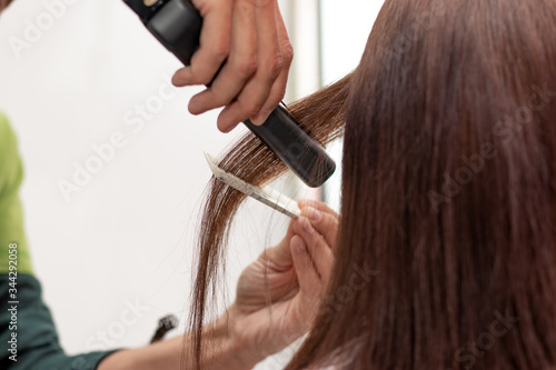  Professional hairdresser straightening the client's hair using a modern flat iron. Making a hairstyle to a young brunette woman at the hairdresser salon