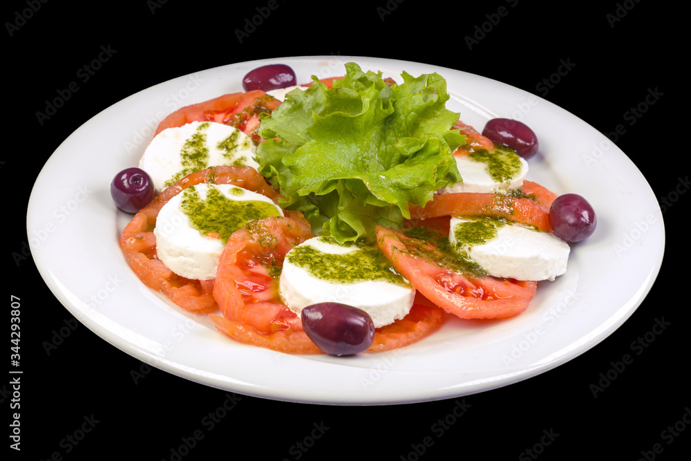 Tasty Caprese salad with peeled tomatoes, mozzarella, basil, and olives, on a plate, isolated on black background