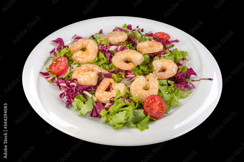 Gourmet shrimp on lettuce and red cabbage on a plate, isolated on black background