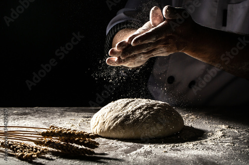 Φωτογραφία Hand clap of professional chef with bowl for cooking and baking utensils with splash flour on dark background
