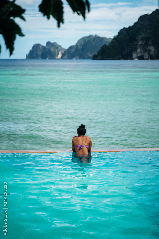 Young woman relaxing in infinity pool looking at beautiful islands in Koh Phi Phi, Thailand