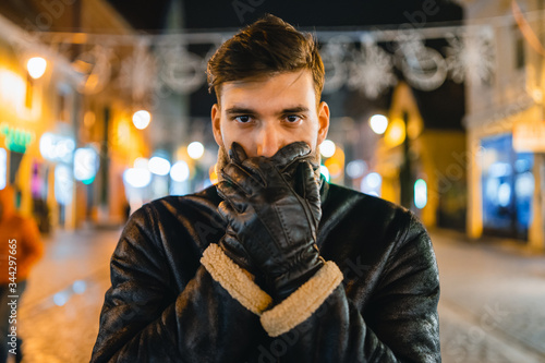 Young male looks at camera while covering his mouth to symbolize cold or repress in a urban environment