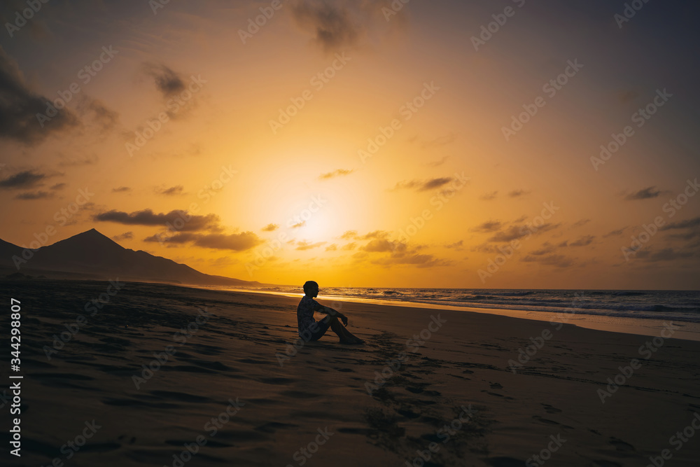 Young male silhouette standing on Cofete beach in Fuerteventura at sunset with beautiful golden hour