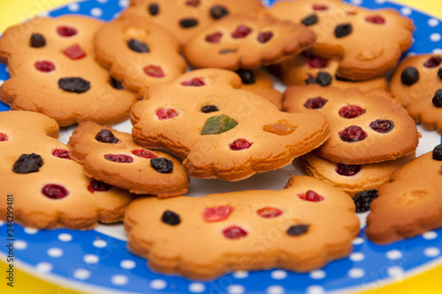 Homemade cookies decorated with berries, raisins and colored candied fruits on a blue plate at yellow background