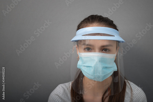 Prevention and protection against the spread of viruses and diseases. Young woman in a protective mask screen with a visor on a gray background
