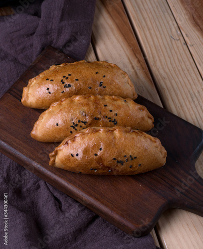 Traditional Russian pies in a wooden tray on a dark rustic background. Russian pirozhki ,baked patties. Top view, copy space, flat lay. buns potatoes and dark napkin. photo