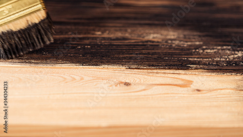 Painting a wooden surface stain. Wooden boards are half covered with stain. A brush with a wooden handle, natural bristles on a background of painted wooden planks. The painting process, the layout.