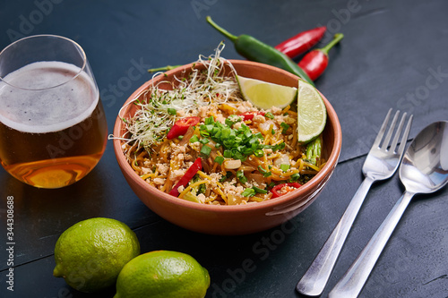 Fotografi Plate with spicy noodles with a glass of beer on a dark wooden table