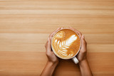 Caramel Macchiato coffee in hand with nice and presentable plating in a white mug top view in wooden table background. Hot beverage photography with space available for text.