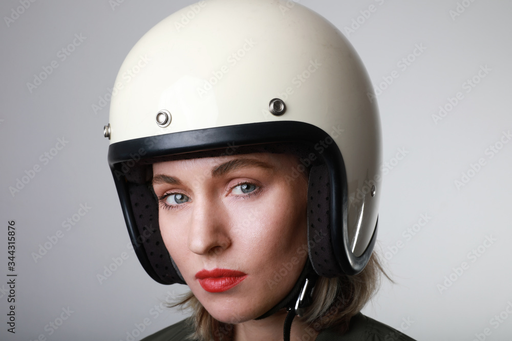 Portrait of biker young woman, wearing white helmet, looking straight at the camera with red lips. Studio background. Portrait of biker young woman, wearing white helmet, looking straight at the camera with red lips. Studio background.