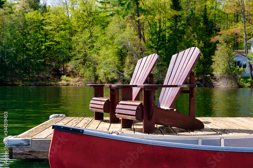 Fotografie, Obraz Two Adirondack chairs on a wooden dock facing the waters of a lake in Ontario, Canada