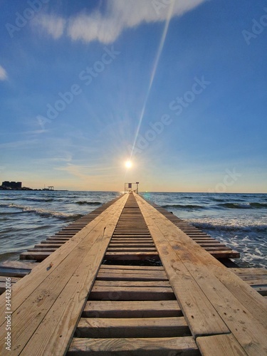 Pier under the rays of the setting sun. Sunset on the Black sea in Anapa, Krasnodar territory. The orange rays of the sun painting the sea in gold color.