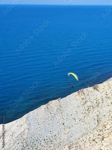 The black sea sparkles under the bright rays of the sun. A hang glider hovers in the sky. The sea is a beautiful deep blue color. View from the top of the mountain.