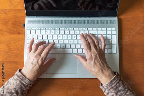 Top view of hands of an old woman using a laptop and a smartphone at home. Concept of old people and technology, keep active...