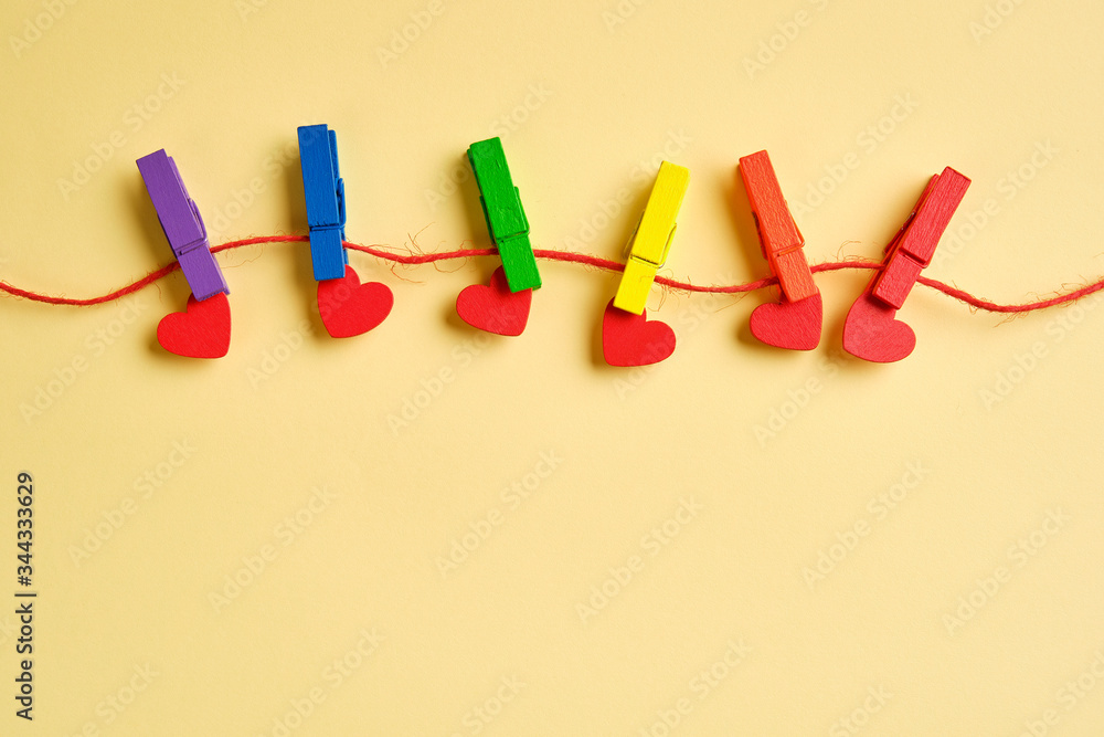 rainbow colored wooden clothespins with clamped red hearts on yellow background. Pride day concept, flat lay, copy space rainbow colored wooden clothespins with clamped red hearts on yellow background. Pride day concept, flat lay, copy space