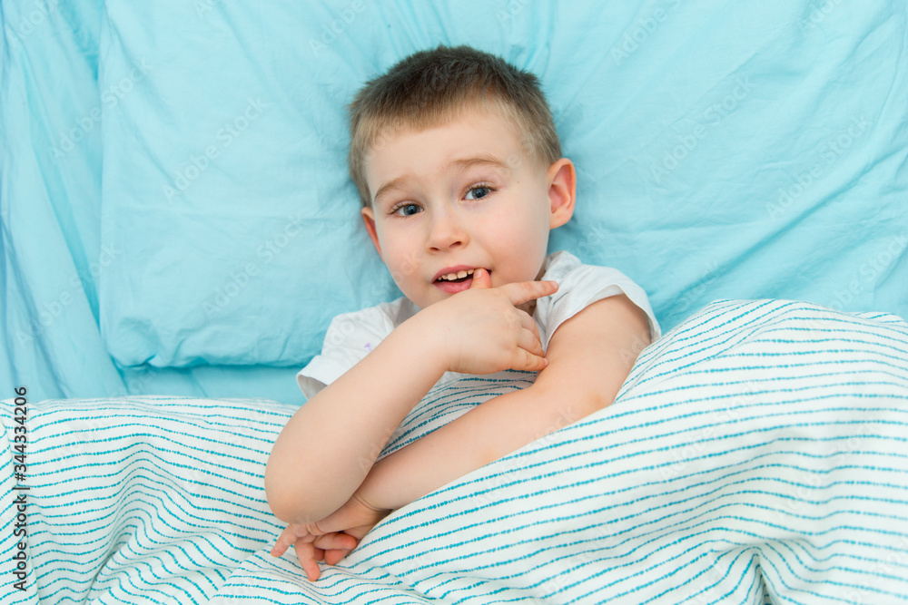 Thoughtful adorable boy in white shirt lays in the bed Thoughtful adorable boy in white shirt lays in the bed