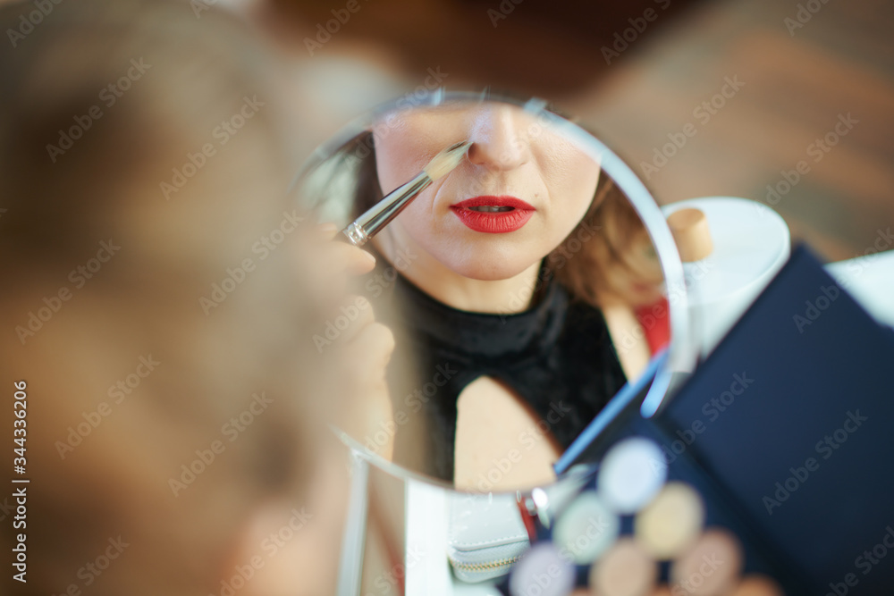 modern woman looking in mirror and using concealer palette