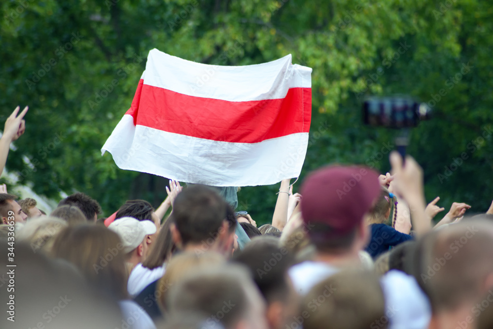 White-red-white flag at a mass event over heads against a background of green foliage of trees. White-red-white flag historical and cultural treasure of Belarus (1918, 1991–1995). White-red-white flag at a mass event over heads against a background of green foliage of trees. White-red-white flag historical and cultural treasure of Belarus (1918, 1991–1995).