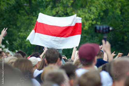White-red-white flag at a mass event over heads against a background of green foliage of trees. White-red-white flag historical and cultural treasure of Belarus (1918, 1991–1995).