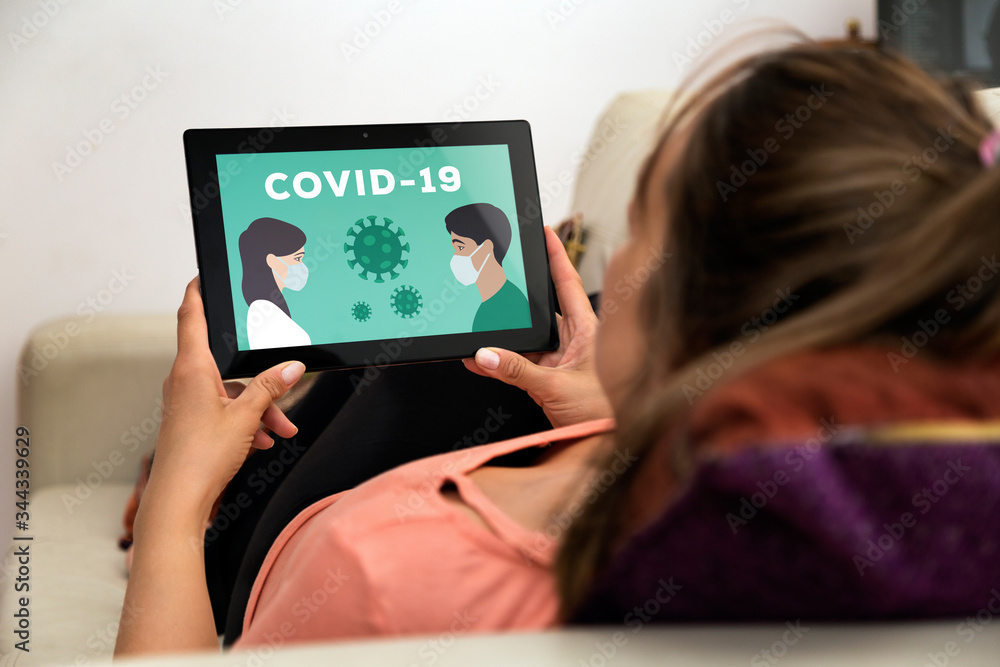 Coronavirus, COVID-19, quarantine time. Woman in home with tablet in her hands. In the screen an illustration of people with medical face mask.