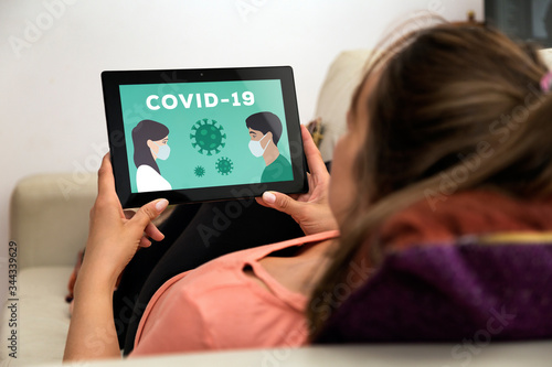 Coronavirus, COVID-19, quarantine time. Woman in home with tablet in her hands. In the screen an illustration of people with medical face mask.
