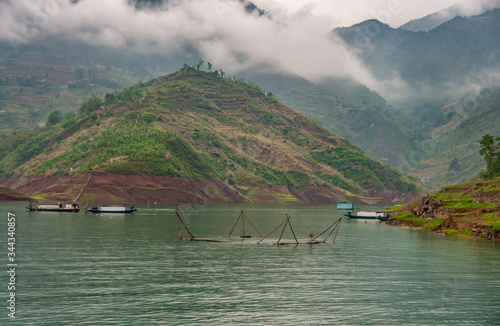 Wuchan, China - May 7, 2010: Dawu or Misty Gorge on Daning River. Fish pens and small boats in emerald green water with tall hills and covered mountains in back.  photo