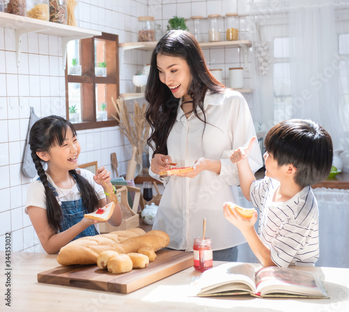 Happy asian family in the kitchen. mother and son and daughter spread strawberry yam on bread, leisure activities at home.