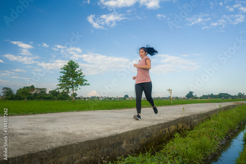 outdoors jogging workout - young happy and dedicated Asian Korean woman running at beautiful ccountryside road under a blue sky on enjoying fitness and cardio activity photo