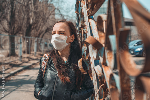 Portrait of young woman in medical mask on her face standing on street. Adult female covered her face with mask to protect yourself from diseases.
