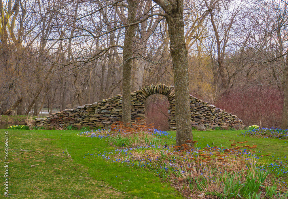 stone wall with arch on a field with early spring flowers
