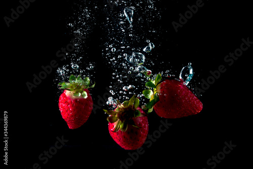 fresh strawberries falling into water leaving splashes